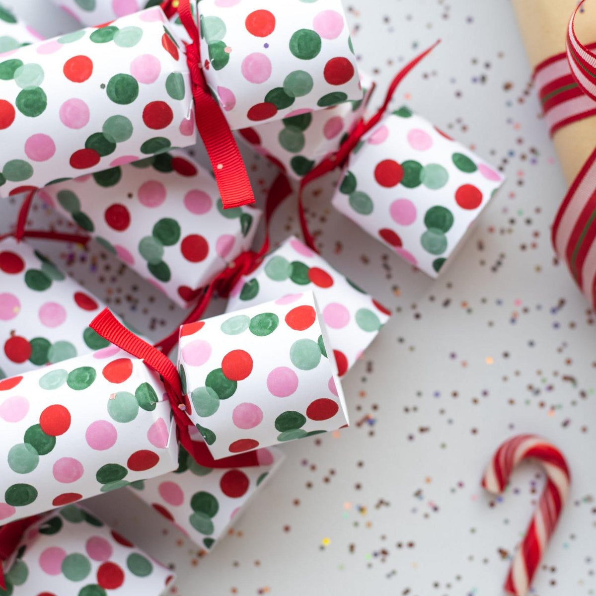 Stack of colourful dotted Christmas crackers with red ribbons and festive styling.