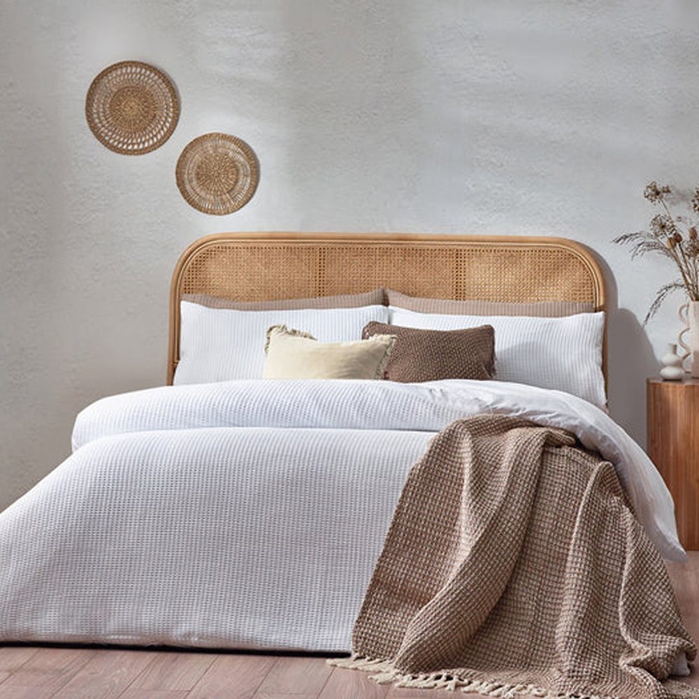 White chunky waffle cotton duvet cover set styled on a bed with a rattan headboard and neutral decorative cushions.