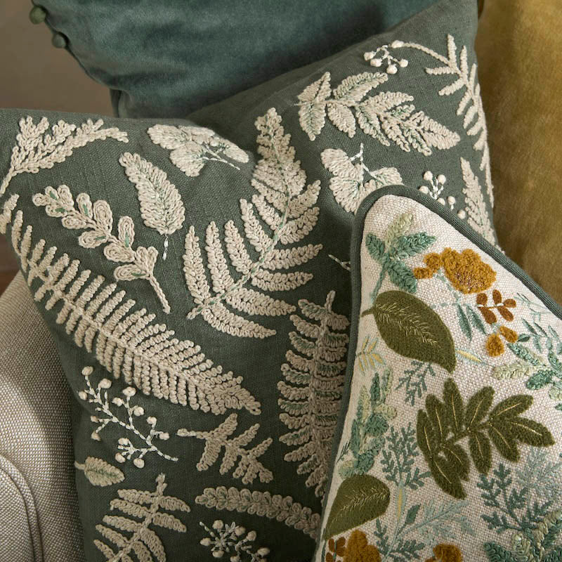 Close-up of the tactile cream embroidery on the eucalyptus cotton Kew cushion, layered with other textiles.