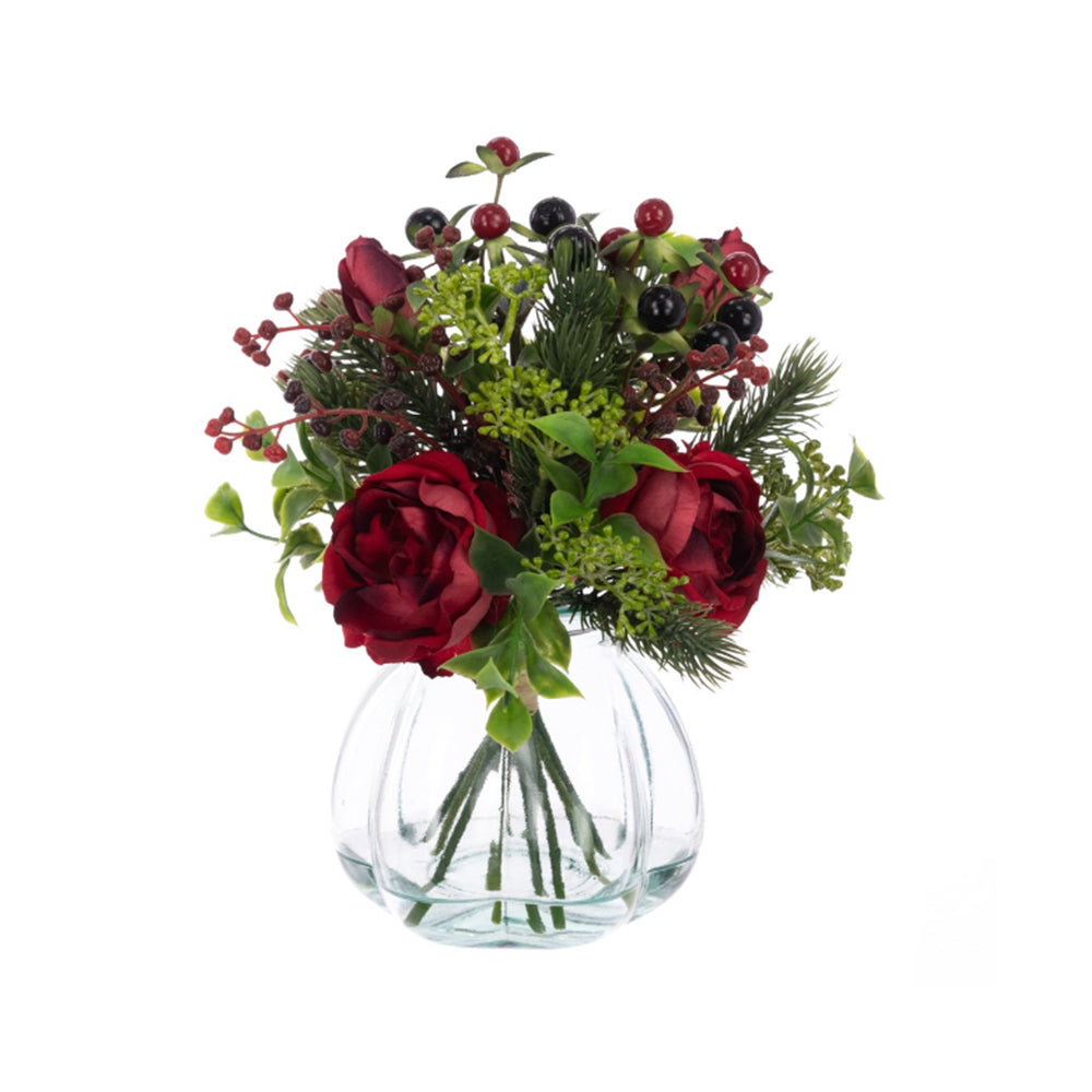 Artificial red roses and dark berries in a ribbed glass vase against a white background.