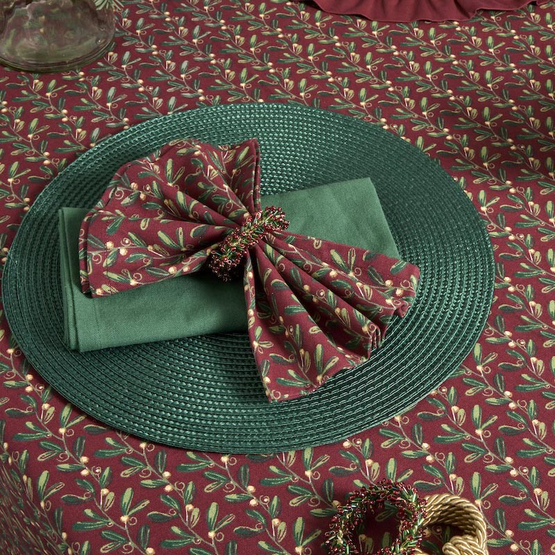 Festive table setting featuring a mistletoe print napkin in a decorative ring on a green placemat