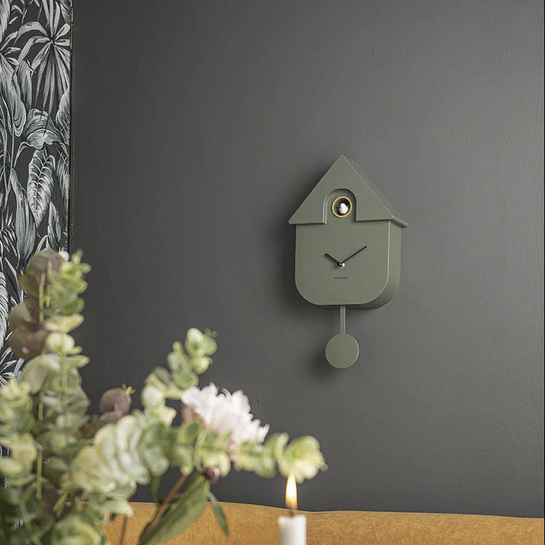 Jungle Green modern cuckoo clock styled on a dark grey wall above a lit candle