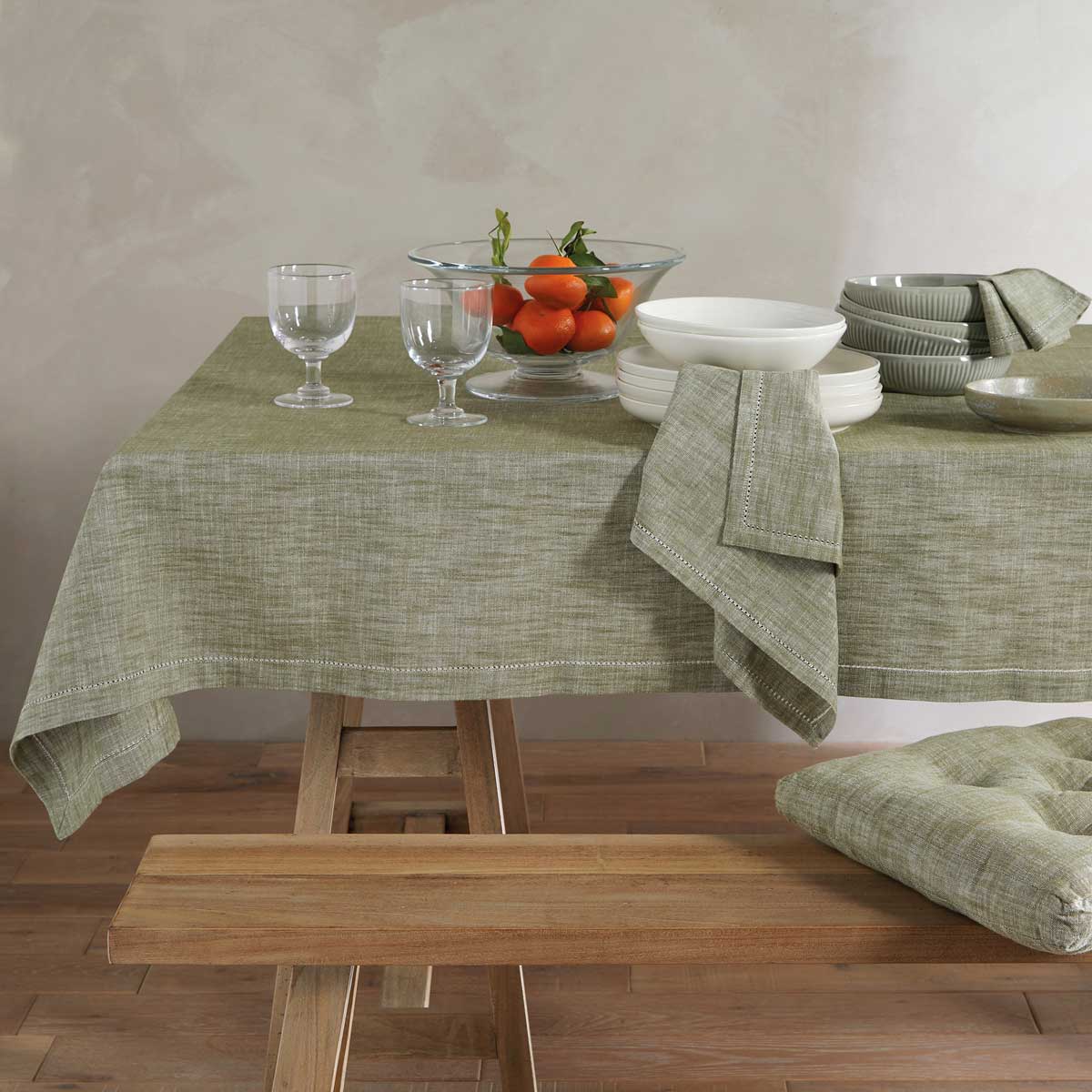 Olive green chambray napkins and matching tablecloth styled on a wooden dining table with white ceramics.