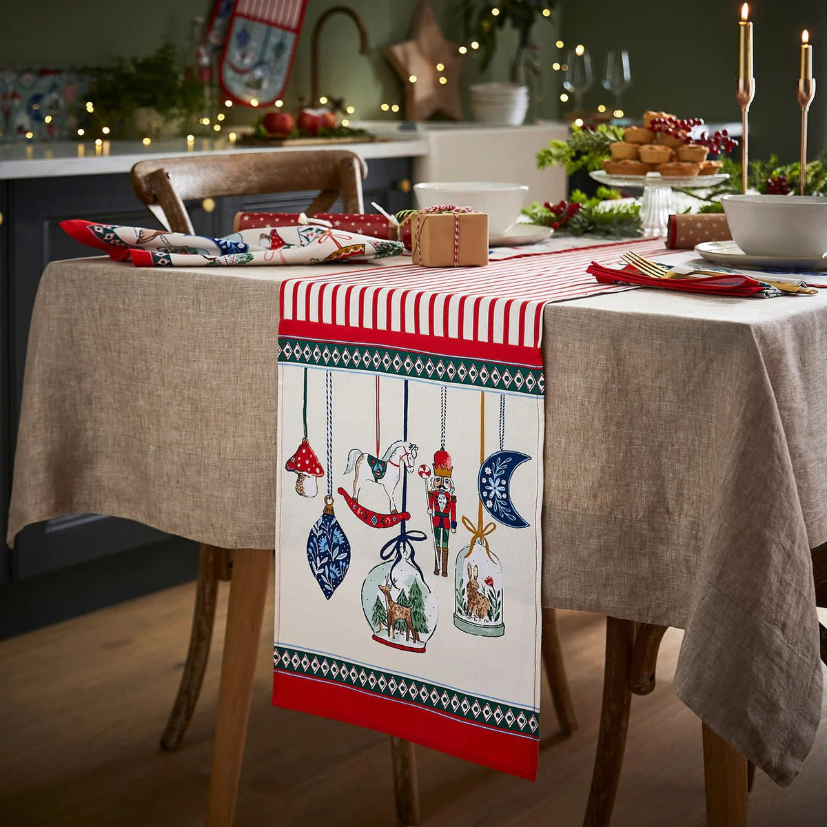 Red and white striped cotton table runner with Nutcracker ornament illustrations on a festive dining table.