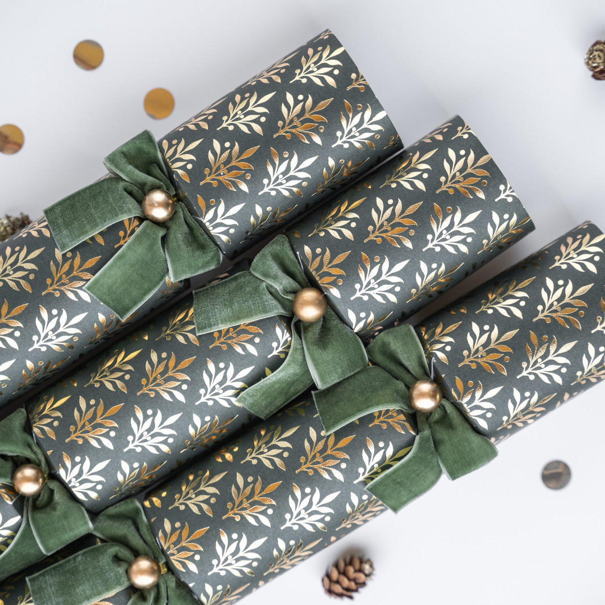 Close-up of three green crackers showing the gold leaf pattern and green velvet bow with gold bead.