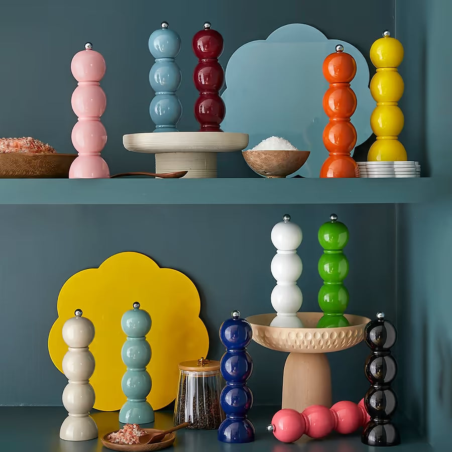 A collection of colourful bobbin grinders in various lacquer finishes styled on kitchen shelves with wooden bowls.