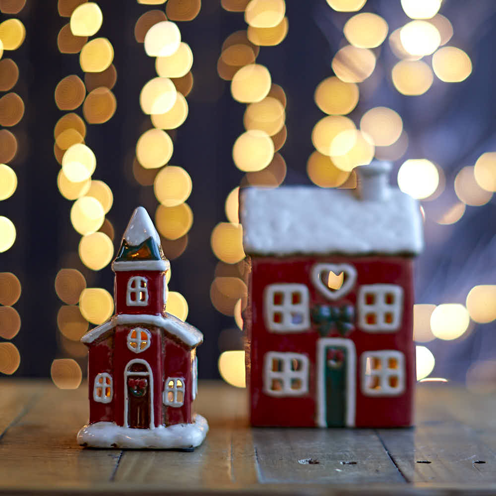 Small church tea-light holder and cottage styled on a wooden surface with festive bokeh lights