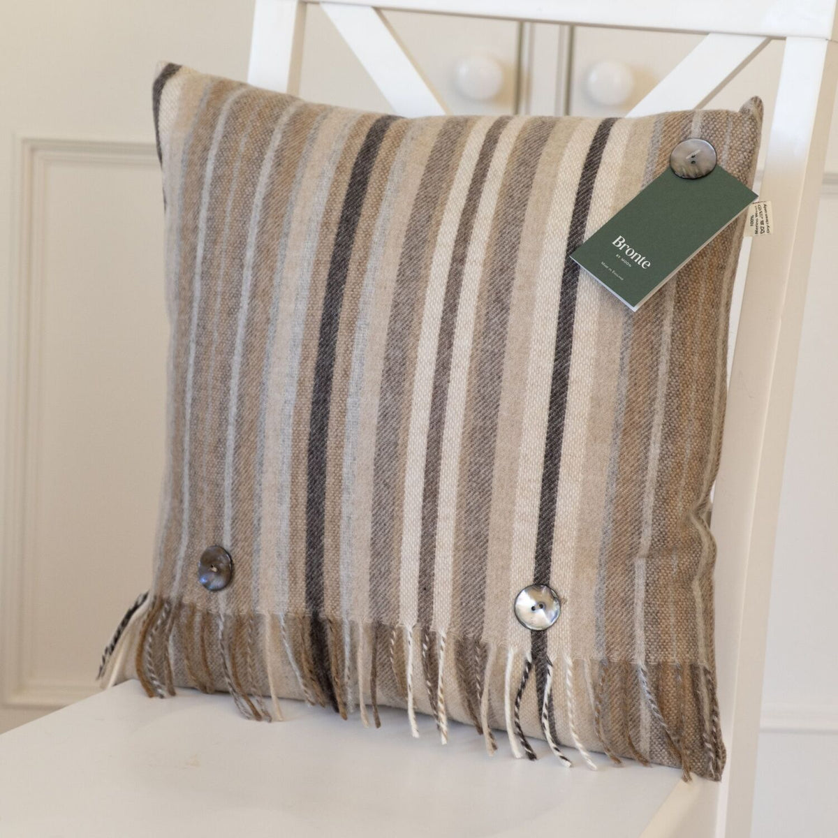 Neutral striped wool cushion with fringe detail, styled on a white wooden chair.