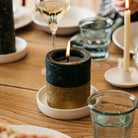 Lit gold-dipped Winter Thyme pillar candle on a white ceramic plate as part of a festive dining table setting.
