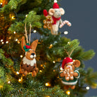 Felt hare Christmas pudding decoration hanging on a lit Christmas tree alongside other character ornaments.