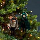 Cloaked mouse felt decoration and a mouse in a winter coat hanging on a lit Christmas tree