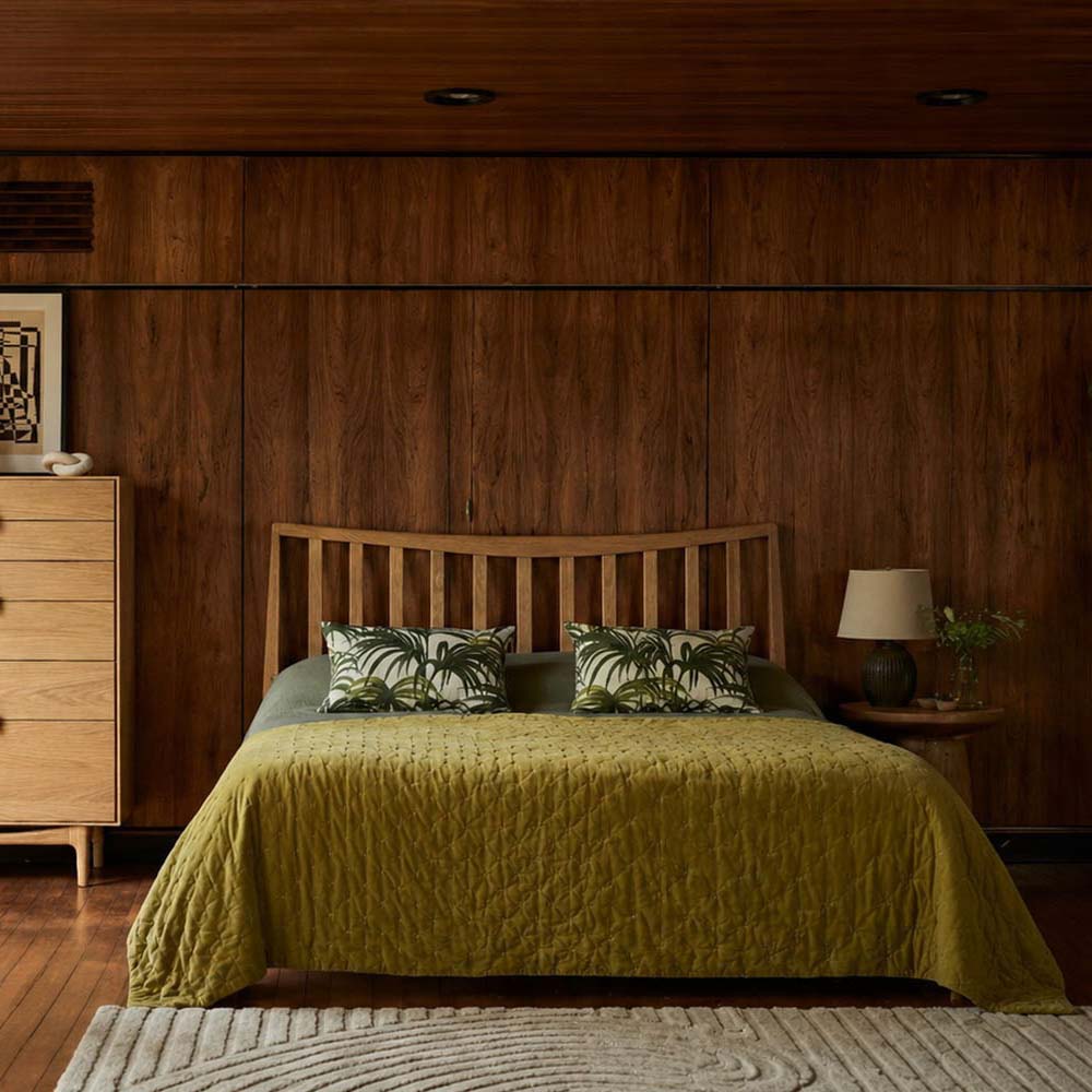 Lifestyle shot of the Larsen oak bed in a dimly lit room with matching chest of drawers