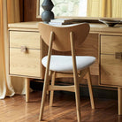 Rear view of an oak bedroom chair tucked under the Larsen dressing table in a room setting.