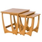 Three graduated oak nesting tables with distinctive curved sculptural bases shown partially pulled out.