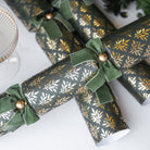 Group of green and gold crackers styled on a white surface with festive decorations.