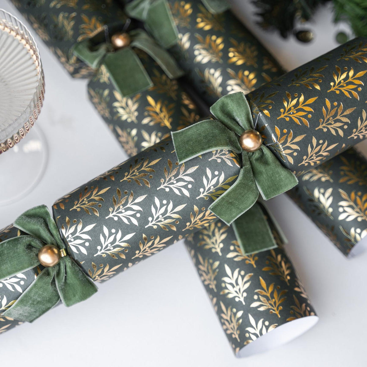 Group of green and gold crackers styled on a white surface with festive decorations.