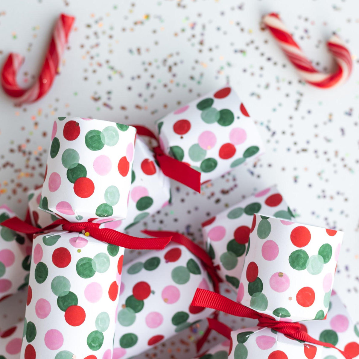 Close-up of confetti dot Christmas crackers on a festive white background with glitter and candy canes.