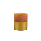Textured orange pillar candle with a metallic gold-dipped base on a plain white background