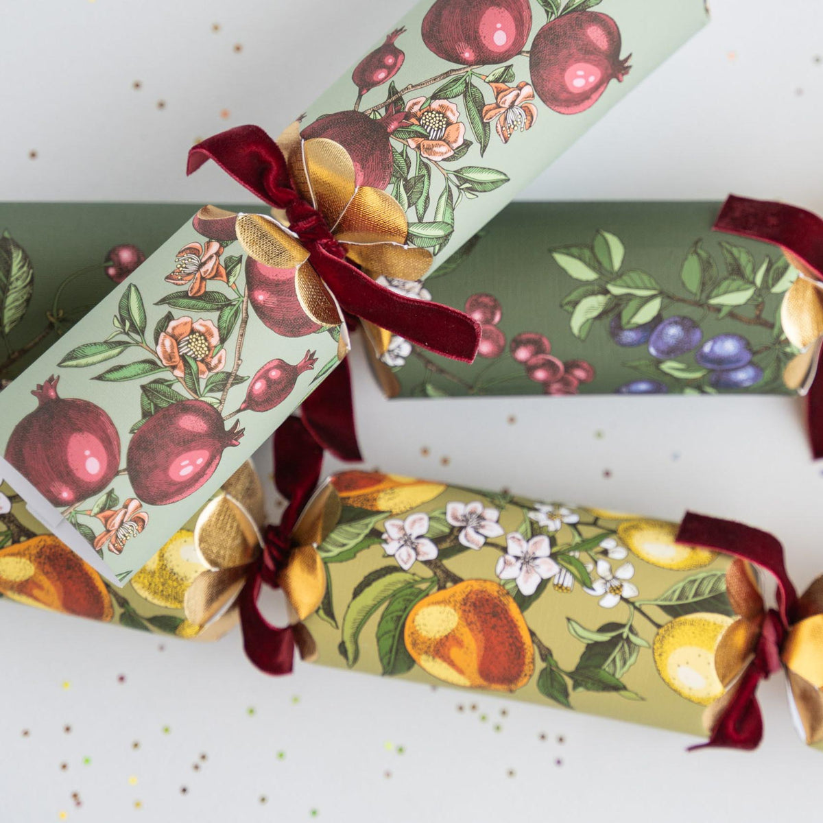 Close up of Christmas crackers featuring botanical pomegranate and lemon illustrations with velvet ties.