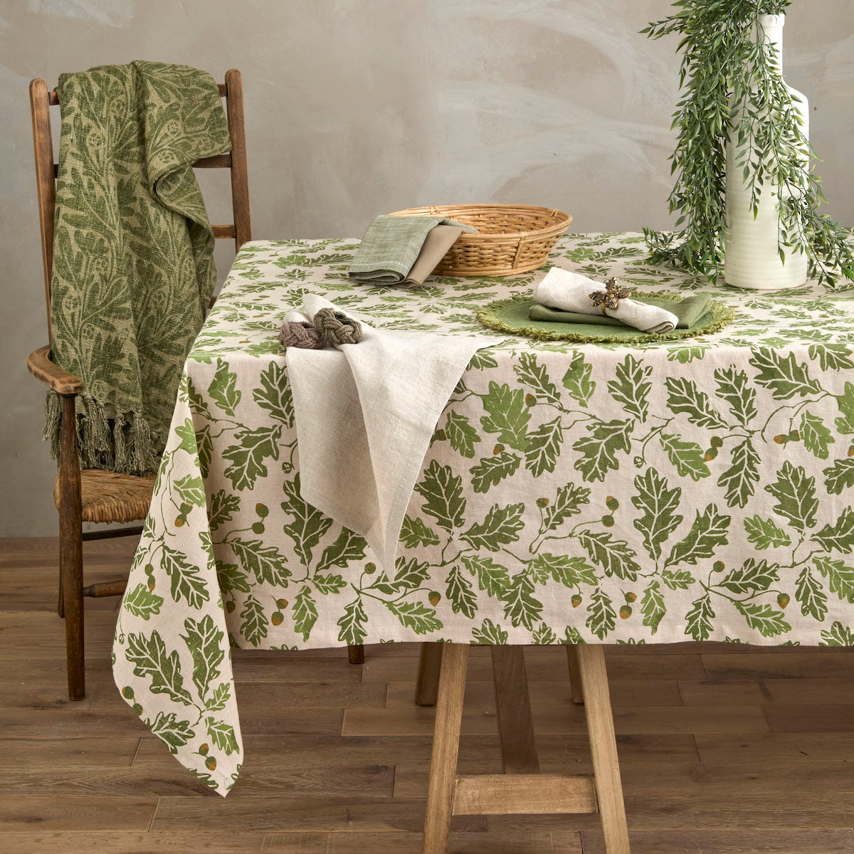 Acorn and oak leaf linen tablecloth draped over a wooden dining table in a rustic room setting.