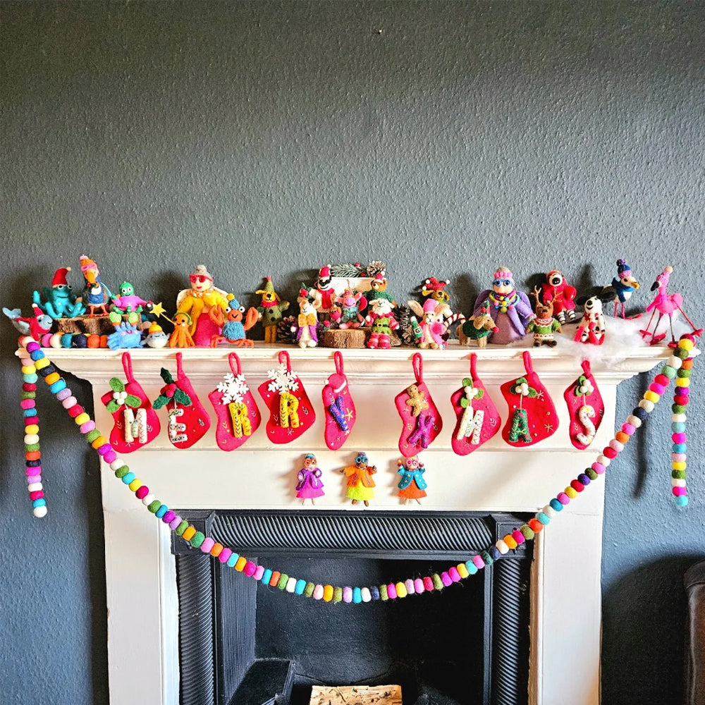 Festive mantelpiece display featuring a row of red alphabet stockings spelling MERRY XMAS