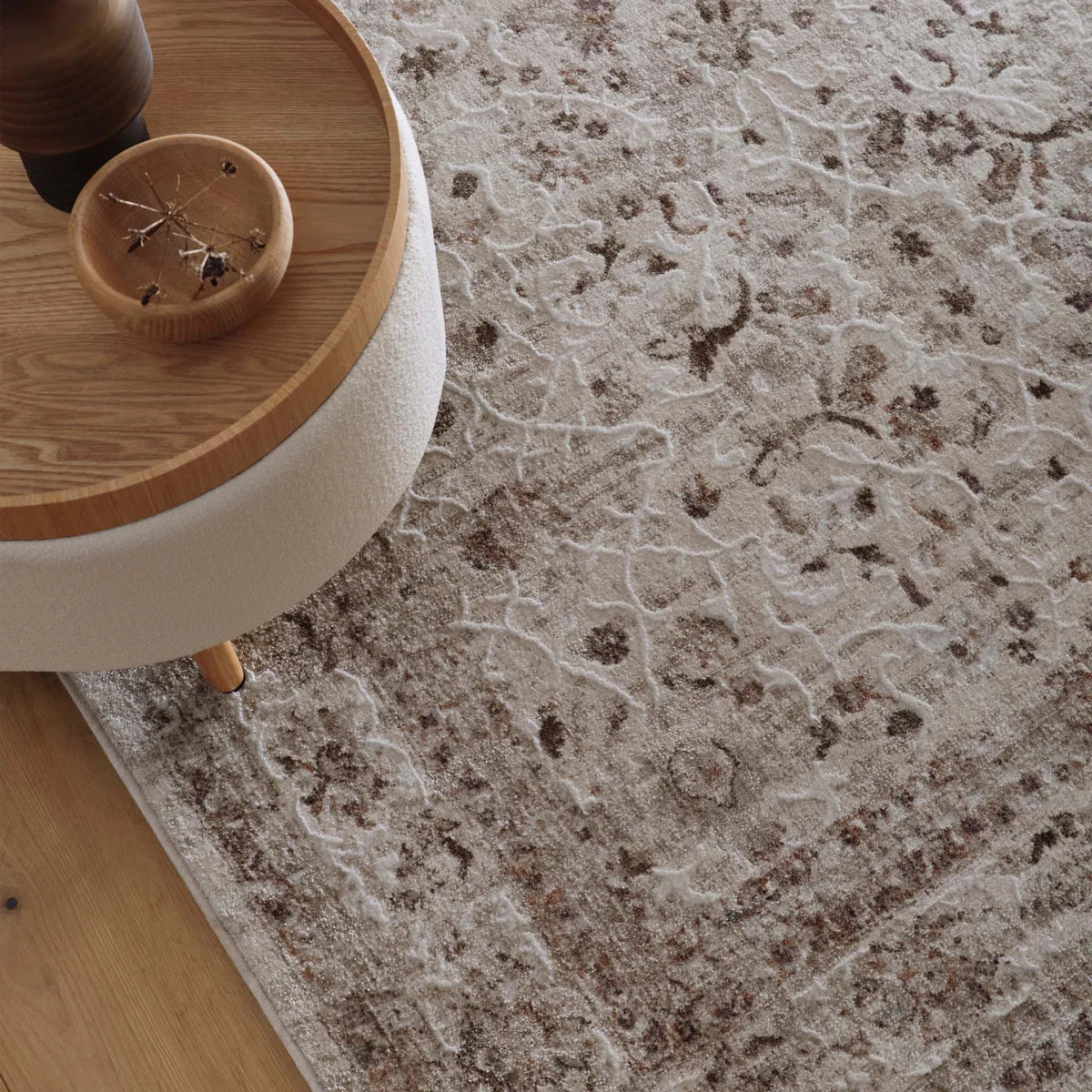 Aurelia Cream rug styled on a wooden floor with a neutral boucle ottoman and wooden tray.