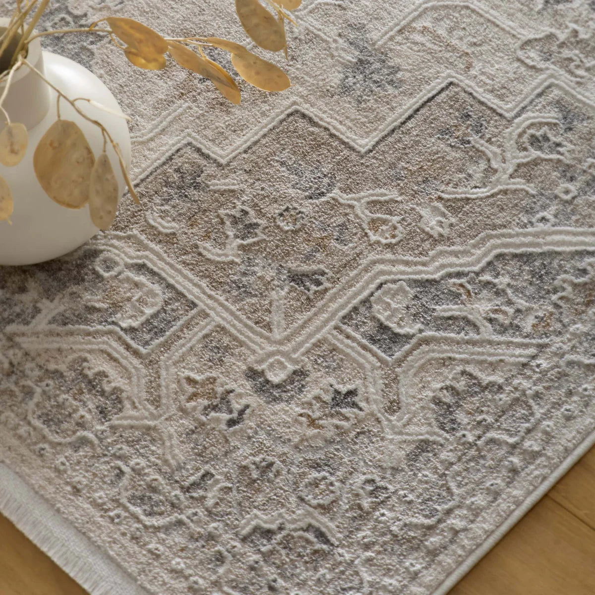 Top-down close-up of the cream rug styled with a white vase and dried foliage.