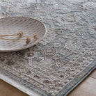 A lifestyle close-up of the Celeste Sea Green rug styled with a ceramic plate on a wooden floor.