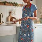 A person wearing the 12 Days of Christmas apron in a festive kitchen, highlighting the front pocket detail.