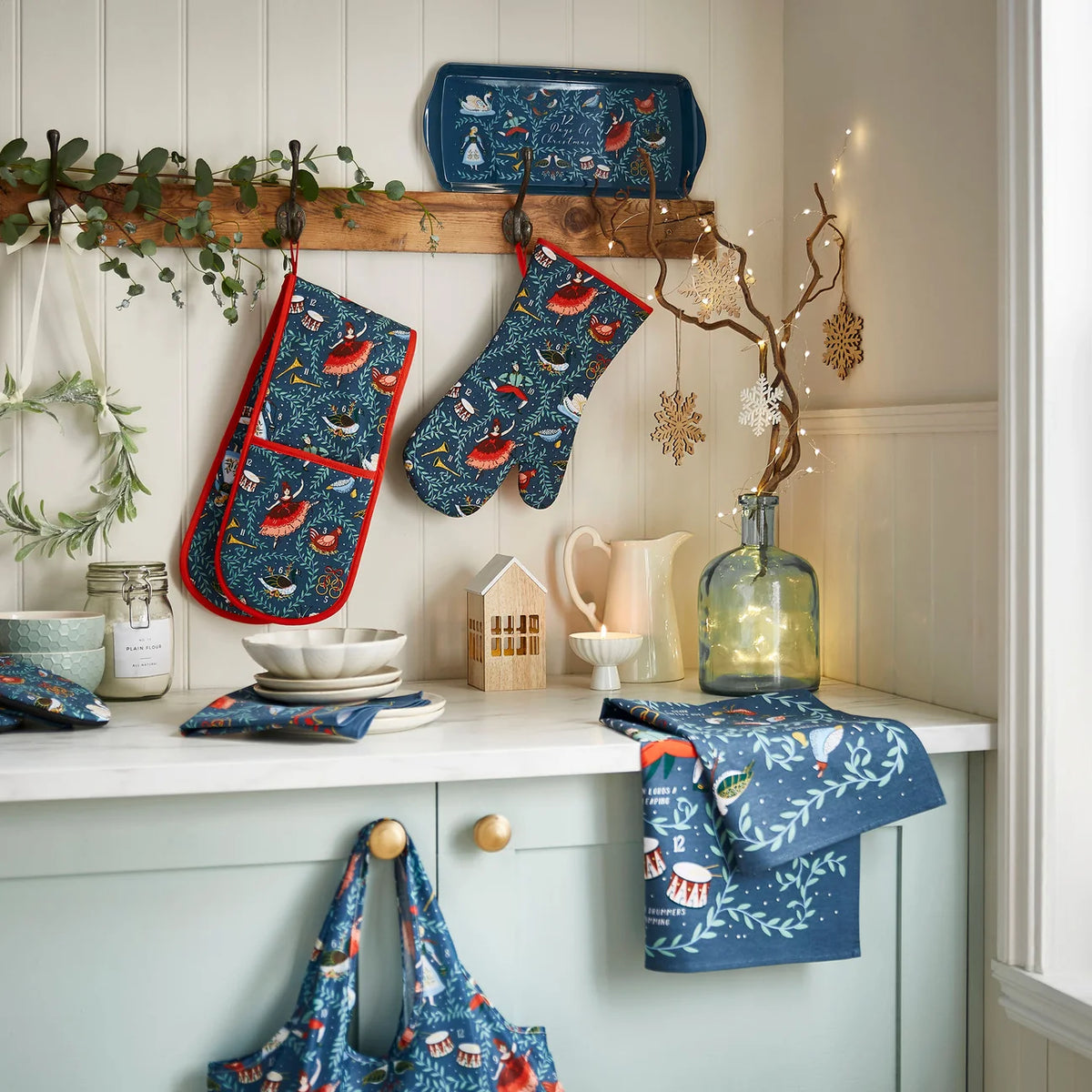 A lifestyle shot of the 12 Days of Christmas kitchenware collection including the apron, oven mitts and tea towel.