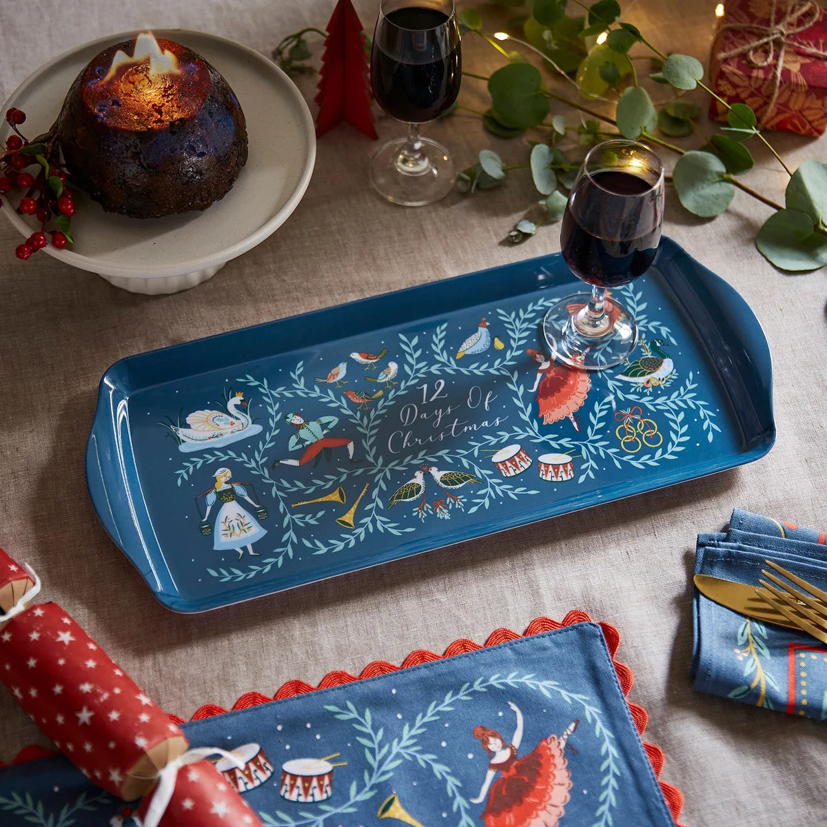 Festive table setting featuring the 12 Days of Christmas tray with a glass of wine and Christmas pudding.