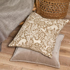 Embroidered woodland cushion styled on a wooden floor alongside a plain velvet cushion and wicker basket.