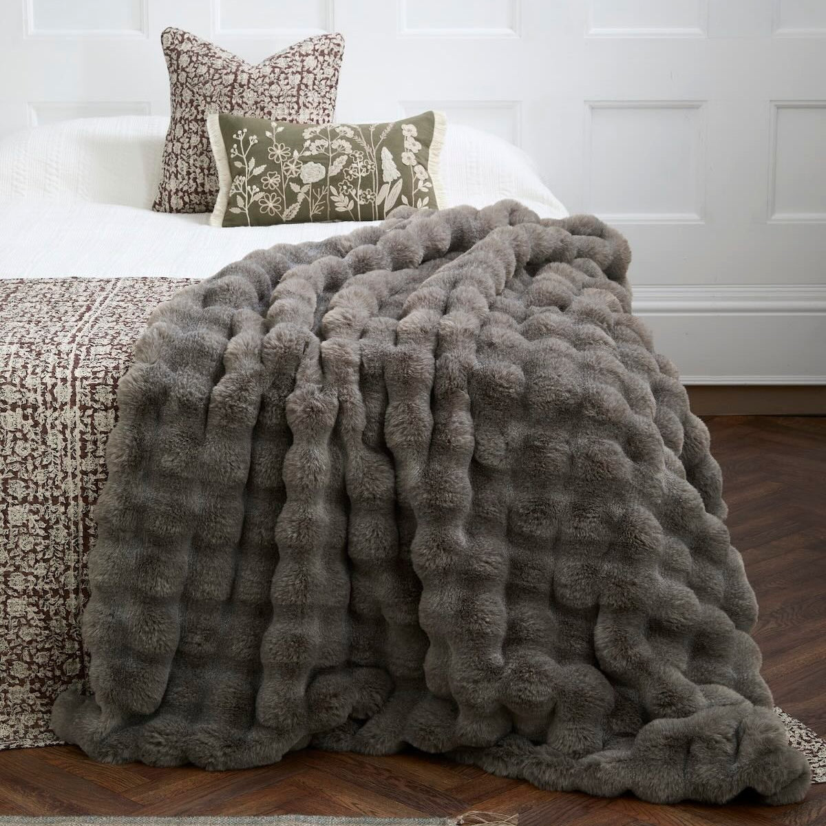 Brown feather-effect faux fur throw draped over the corner of a bed in a bedroom setting.