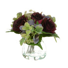 Artificial purple roses and green hydrangeas in a clear curved glass vase against a white background