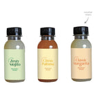 Side-by-side view of three mocktail mixer bottles with black screw caps and simple labels.