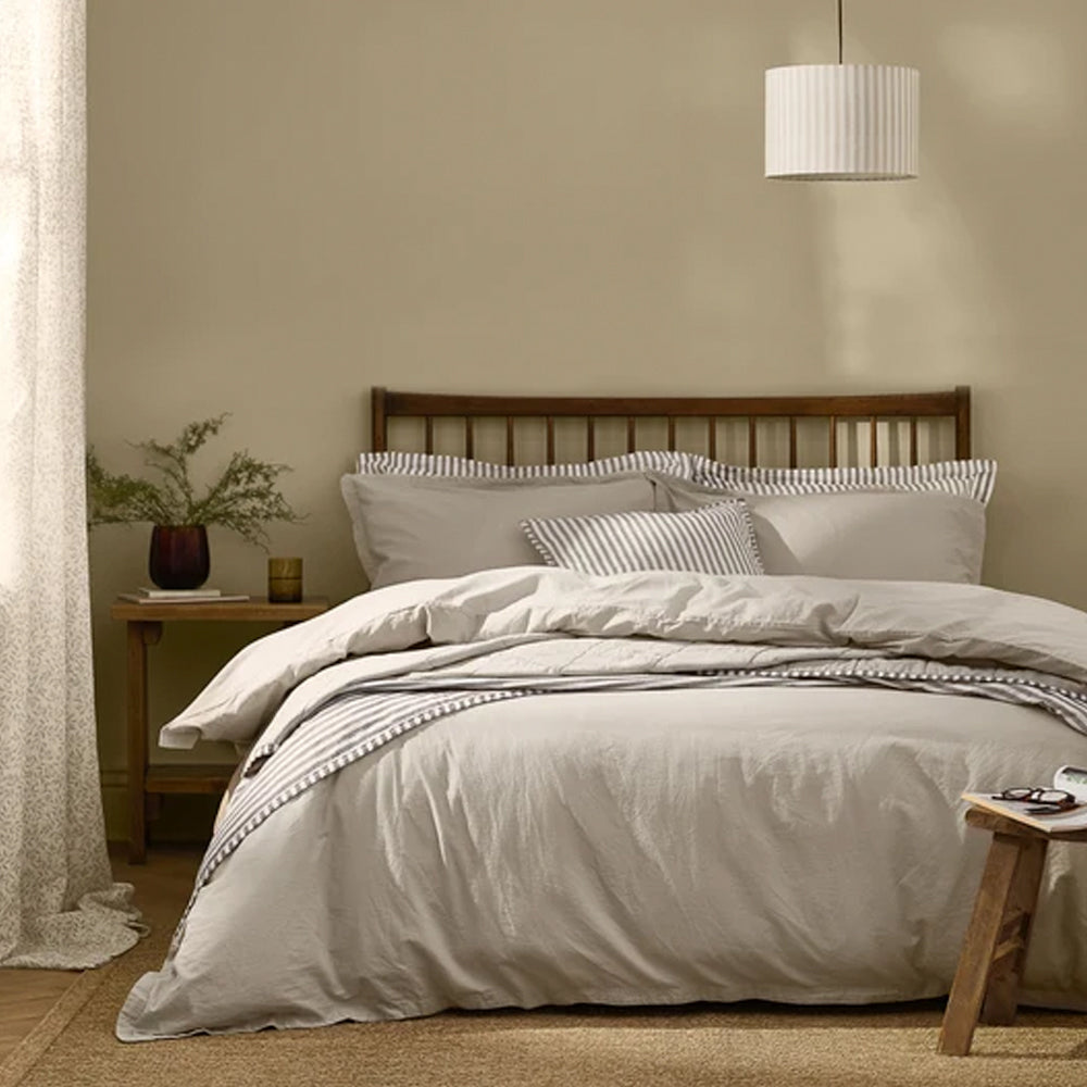 Hebden Washed Cotton Duvet Cover Set in Stone styled on a wooden bed frame with matching pillowcases.
