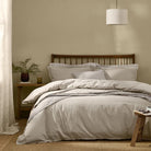 Hebden Washed Cotton Duvet Cover Set in Stone styled on a wooden bed frame with matching pillowcases.