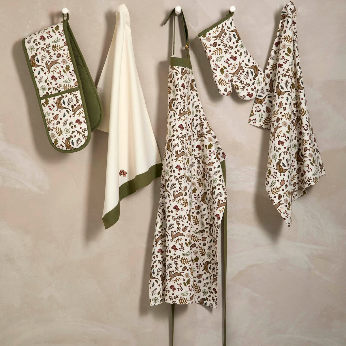Into the Woods kitchenware collection including tea towels, apron, and oven gloves hanging on pegs.