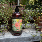 The botanical hand wash bottle styled outdoors on a lead surface surrounded by lush garden greenery.