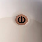 Close-up of the power button icon on top of the cappuccino lacquered lamp shade.