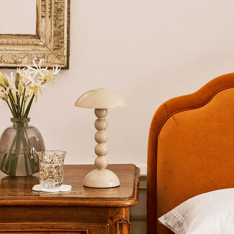 The cappuccino bobbin lamp styled on a dark wood bedside table next to an orange velvet headboard.