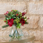 Faux rose and berry arrangement in a glass vase, styled on a gold side table against a stone wall.