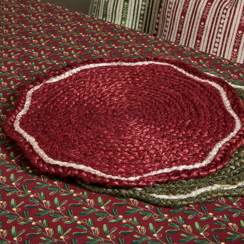 Red scalloped jute placemat styled on a festive patterned tablecloth alongside a green variant.