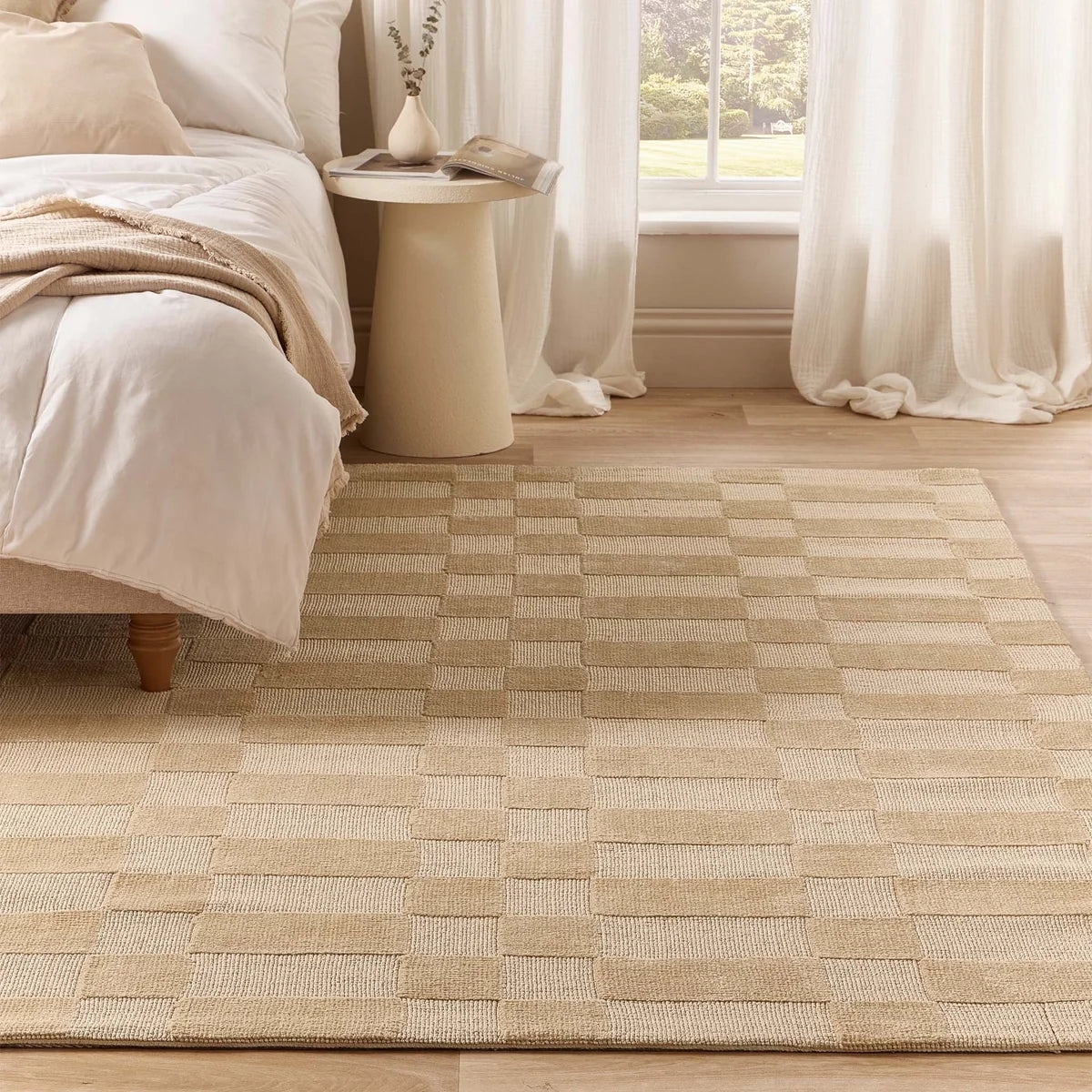 Soho Beige rug styled in a bedroom setting beside a bed with white linens and light wooden flooring.