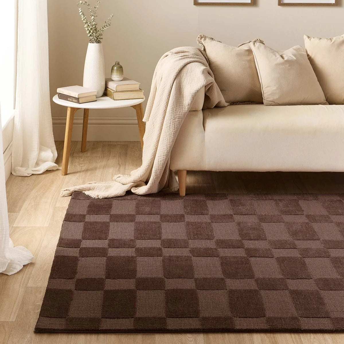 Origins Soho Chocolate rug styled in a living room beside a cream sofa and wooden floor.