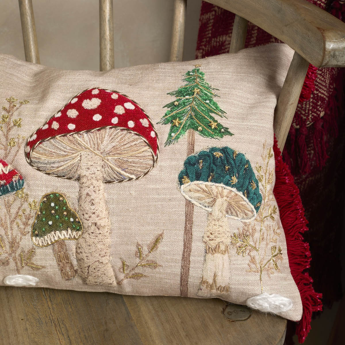 Close-up of the textured embroidery on the toadstool cushion showing the green trees and red fungi details.