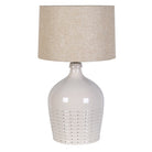 Pale off-white ceramic table lamp with a pierced dotted base and natural linen shade against a white background.