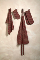 Festive kitchen textiles including a mistletoe print tea towel, oven gloves, and apron hanging on a wall.