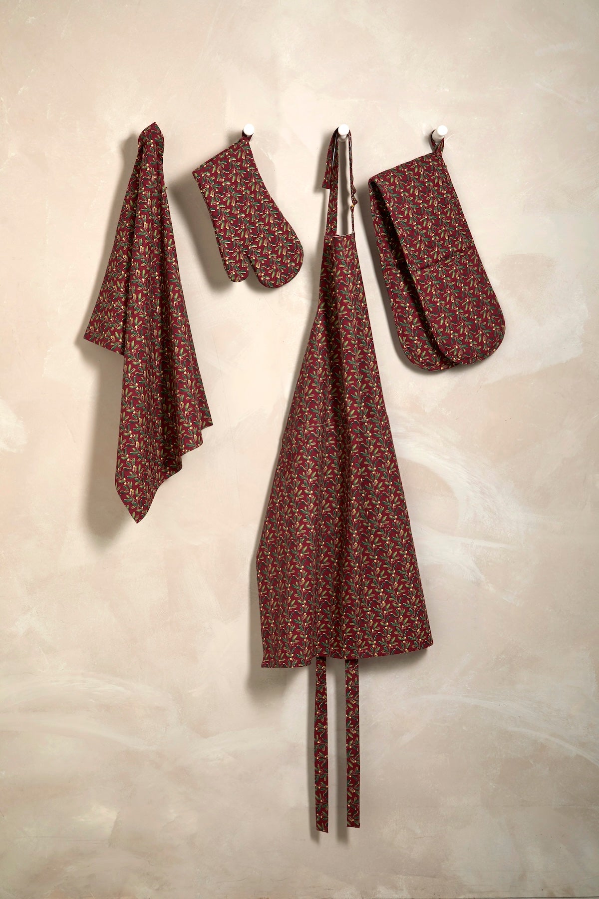 Festive kitchenware collection including the Under the Mistletoe apron, oven glove, and tea towel hanging on hooks.