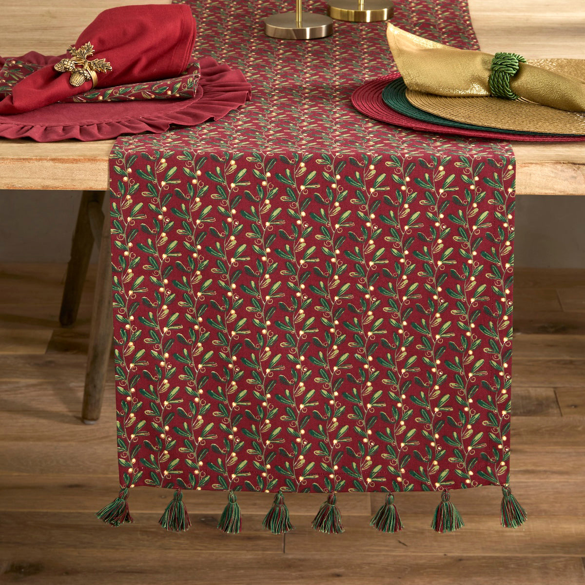 Festive red mistletoe table runner styled on a wooden dining table with napkins and Christmas place settings.